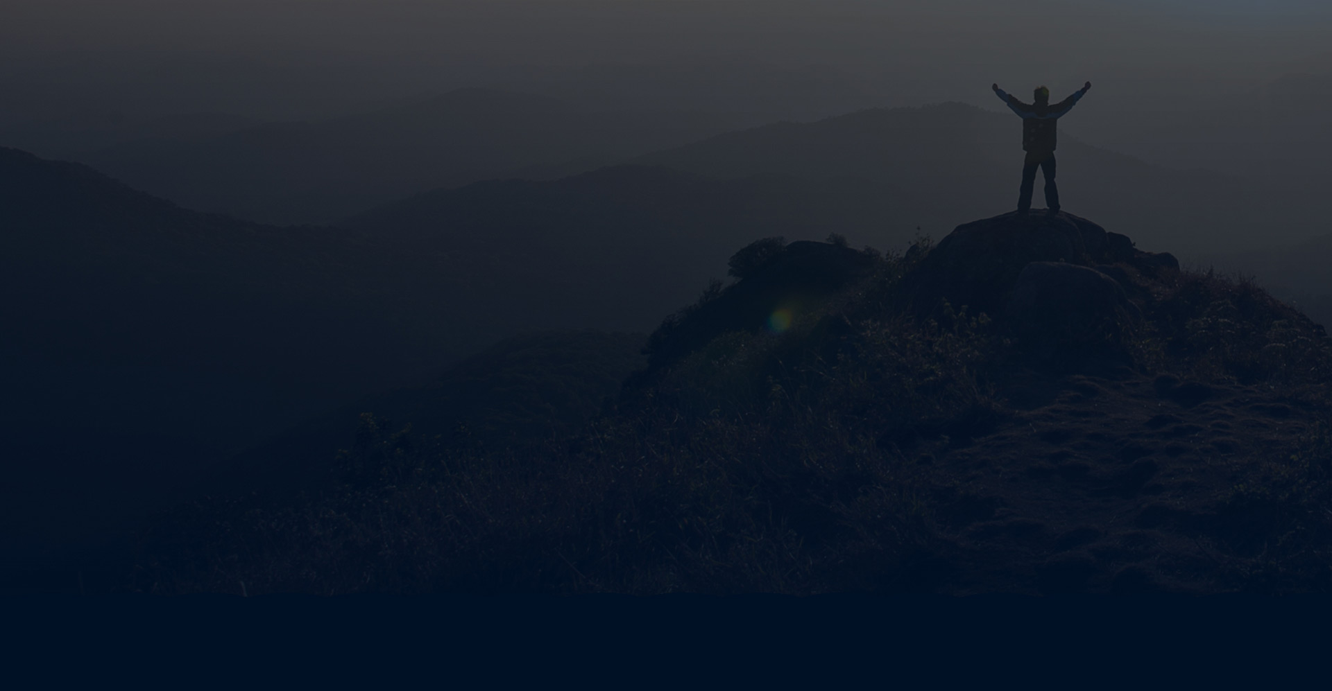 Man stands on top of mountain with arms raised in triumph